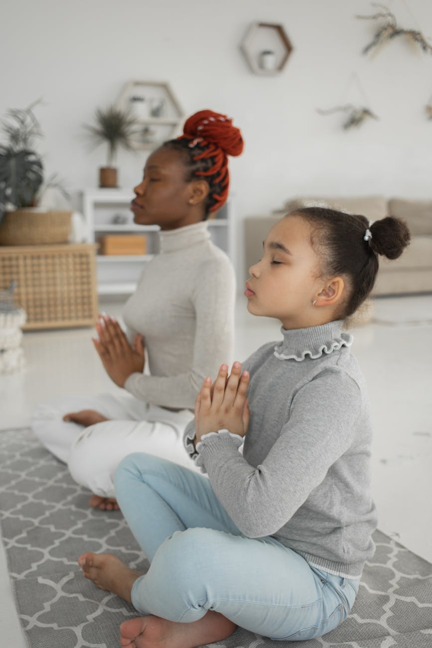 young black woman with cute daughter meditating with closed eyes at home